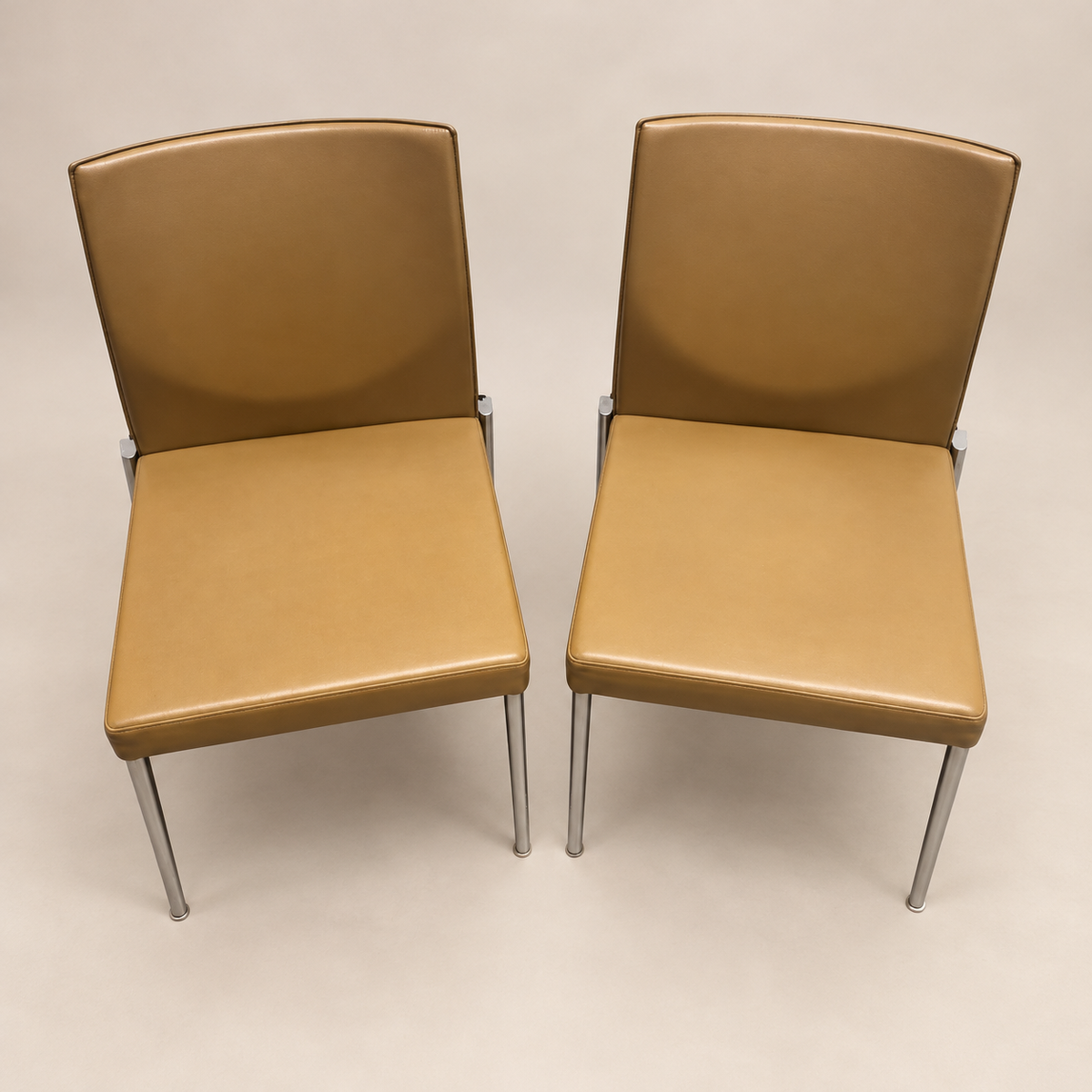 Two matching caramel-tan KFF upholstered armless high-back chairs with slim chrome-finish legs, actual-item hero
